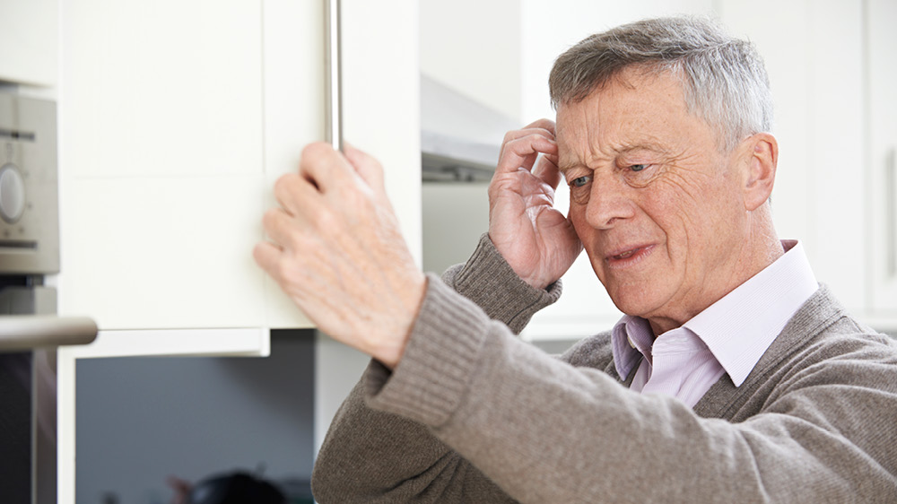 Older gentleman opening a cabinet, looking confused